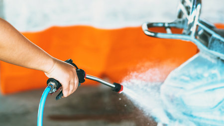 Happy woman washing self-service her motorcycle or motorbike at automatic coin-operated car wash machine. Cleaning of motorcycle or scooter at car wash by water and foam. Selective focus on hands.の写真素材