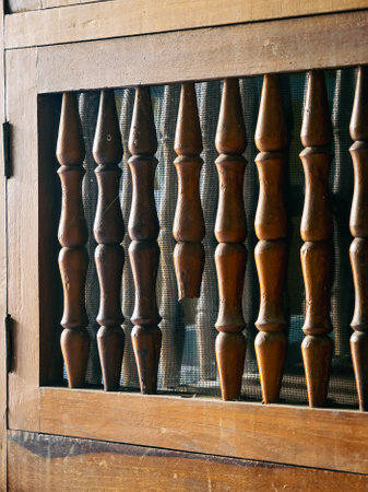 Old lattice balustrade of wooden cupboard. Old railing of folding door with wire mesh in background of wooden cupboard or cabinet. Wooden railings missing, leaving gaps.の写真素材