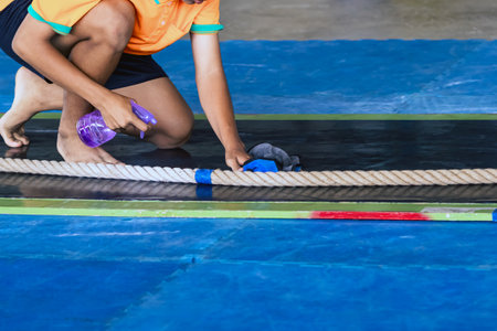 Male athlete assistant using cleaning solution and towel to wipe on floor of tug of war area to prevent slipping before the tug of war competition. Wiping and cleaning to prevent slipping and falling.の写真素材