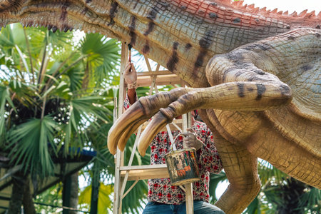 Male painter stands on a ladder and uses a brush to paint and decorate a large dinosaur statue or sculpture to make it beautiful and realistic. Creating realistic art and coloring of dinosaur skins.の写真素材