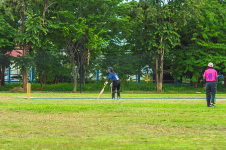 Asian young female cricket player wear protective gear and hitting ball with bat on field. Woman teenager playing cricket in park. Girl with bat and ball on cricket pitch. Sports activity and exerciseの写真素材