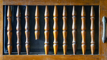 Old and broken lattice balustrade of wooden cupboard. Old broken railing of folding door with wire mesh in background of wooden cupboard or cabinet. Wooden railings broken and missing, leaving gaps.の写真素材