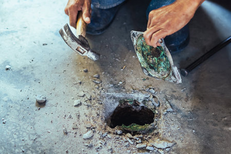 Elderly worker of water utility maintenance service change sewer manholes in house. Hands of old man changing and repairing brass sewer cover of sewerage system. Maintenance of toilet drainage system.の写真素材
