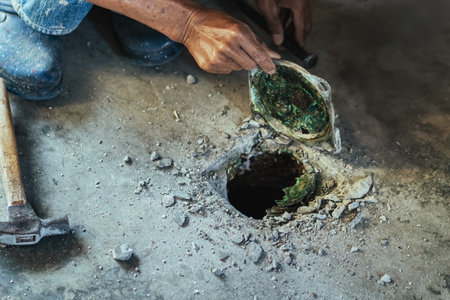 Elderly worker of water utility maintenance service change sewer manholes in house. Hands of old man changing and repairing brass sewer cover of sewerage system. Maintenance of toilet drainage system.の写真素材