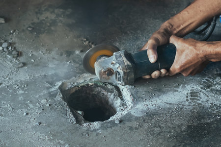 Worker of water utility maintenance service using angle grinder to change sewer manholes in house. Old man change and repair brass sewer cover of sewerage system. Maintenance of toilet drainage systemの写真素材