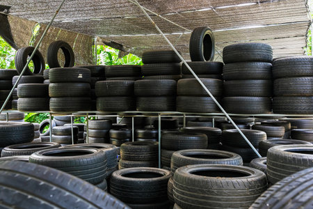 Old used many tires stacked with high piles in car repair shop. Piles of old black rubber tyres. Pile of pneumatic tyres background. Warehouse of old tires for recycling. Vehicle part. Wheel tyresの写真素材