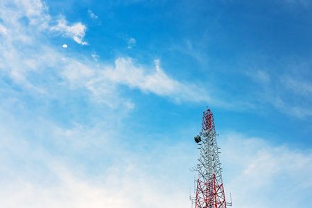 Mobile phone tower, base station or monopole with the moon in clear blue sky background. Antenna...