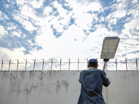Asian elderly electrician man installing solar powered motion sensor light on cement or concrete wall background. Old man Install or mount solar lights on wall with beautiful sky for stree light.の写真素材