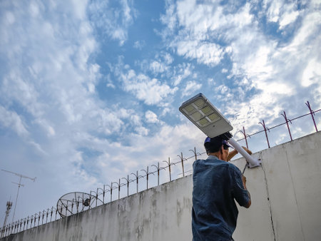 Asian elderly electrician man installing solar powered motion sensor light on cement or concrete wall background. Old man Install or mount solar lights on wall with beautiful sky for stree light.の写真素材