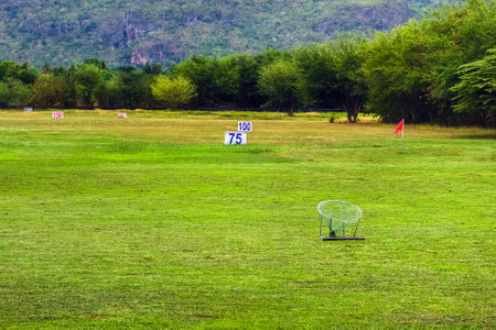 View of golf driving range with grassy slopes and distance signs with beautiful natural tree fence and mountain. A driving range shot showing yardage signs. Yard signs in driving range and golf ball.の写真素材