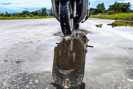 People ride motorcycle passing through puddles after heavy rain. Motion motorcycle rain dirty puddle of water spray from the wheels. Motorbike moped rides through a puddle on wet road in the rain.の写真素材