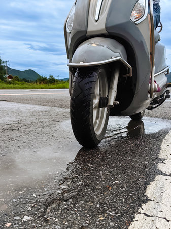 People ride motorcycle passing through puddles after heavy rain. Motion motorcycle rain dirty puddle of water spray from the wheels. Motorbike moped rides through a puddle on wet road in the rain.の写真素材