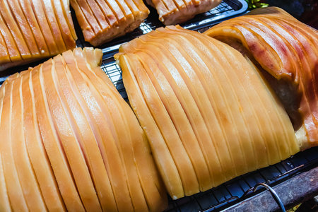Pork belly with scored skin resting on tray to dry in sun, showing gelatinous layers and golden tones. Ideal for cooking process or food prepare concept. Process of making delicious crispy pork.の写真素材