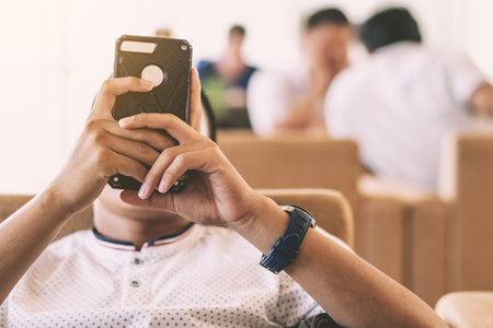 Hands of male tourist using mobile smartphone with suitcase traveling while waiting for flight in Airport Terminal hall. Hands of man uses cell phone while waiting to board a plane at departure gate.の写真素材