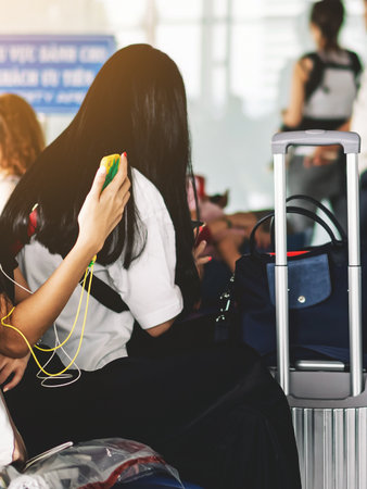 Hands of female tourist using mobile smartphone with suitcase traveling while waiting for flight in Airport Terminal hall. Hands of woman uses cell phone while wait to board a plane at departure gate.の写真素材