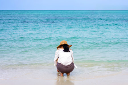 Back view portrait of beautiful young woman wear floppy hat relax leisure at beach sea ocean on travel vacation trip. Woman in straw hat sitting and resting on beach. Happy summer lifestyle concept.の写真素材