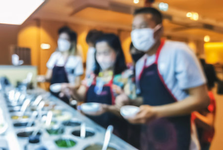 Blurred image of people or customers wear face masks and aprons line up to get buffet food at restaurant. People serving themselves in buffet. People choose to eat food accord to their own preferencesの写真素材