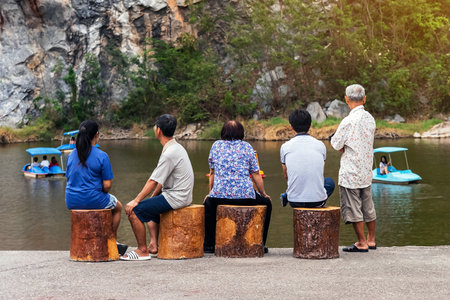 Back view of family relaxing together by the lake with blurred image of happy people enjoying pedal boats or water bikes in lagoon with beautiful canyon in background. Happy family holidays outdoors.の写真素材