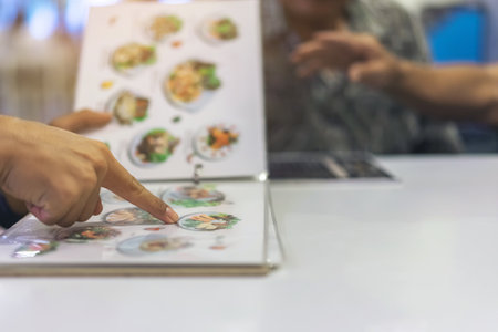 Close up to man finger with menu choosing dishes at restaurant. A person reading menu at table....