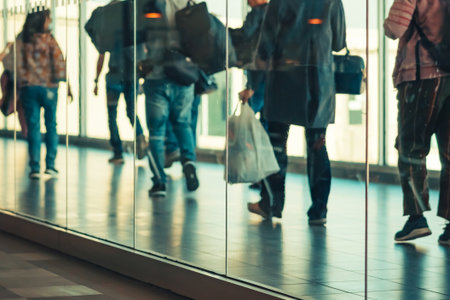 Photograph through large clear glass wall with blurred image of departing passengers and luggage...
