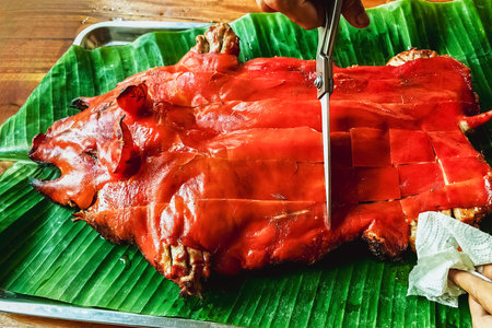 Chef hand cuts piece grilled pork in steaks with scissors. Traditional roasted suckling pig cooked on banana leaf in tray. Divide the roast pork into portions. Cut Barbecued suckling pig into pieces.の写真素材