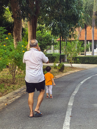 Back view of elderly father and little son or grandfather and grandson walking together at garden. Middle age father with son or senior grandfather with grandchild spending time together in park.の写真素材