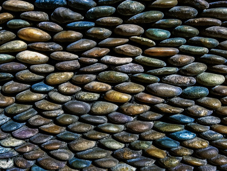 Beautiful wall stacked with stones of various sizes. Smooth pebbles background. Variety of smooth, natural rocks with different shapes and textures. River stone or gravel fence background or wallpaperの写真素材
