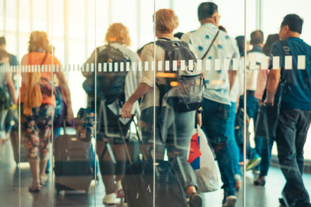 Photograph through large clear glass wall with blurred image of departing passengers and luggage walking airplane boarding corridor from terminal to plane in background. Selective focus on glass.の写真素材