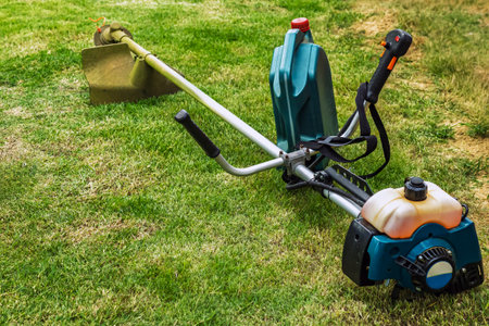 Brush cutter or shoulder strap mower and green gallon of gasoline on lawn with green grass before...