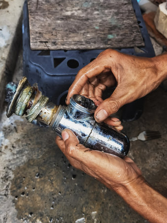 Clogged sink pipe in hands ,A plumber cleans a clogged siphon pipe of a sink in the kitchen. Clogged rusty water trap siphon and drainage pipe cleaning. Home plumbing maintenance service. DIY conceptの写真素材