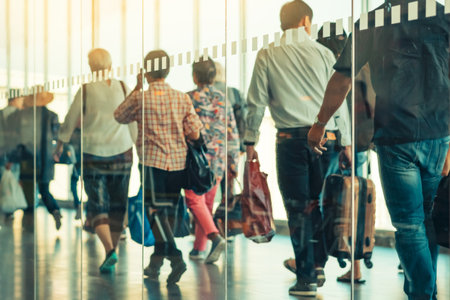 Photograph through large clear glass wall with blurred image of departing passengers and luggage walking airplane boarding corridor from terminal to plane in background. Selective focus on glass.の写真素材
