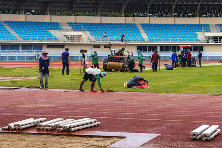 KANCHANABURI, THAILAND-AUGUST 8, 2025 : Unidentified team of landscape workers installing fresh natural sod rolls on prepared soil ground for professional sports field project at Kleeb Bua Stadium.のeditorial素材
