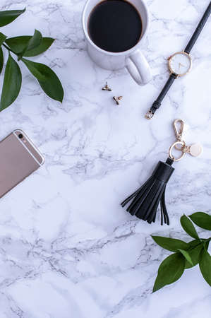 A white mug with black coffee on a white countertop. There are white meringues nearby. A phone, a black hat and black womens accessories. Top view.の写真素材