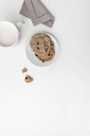 A white mug with milk on a white countertop. There is a napkin next to it and one cookie on a plate. Top viewの写真素材