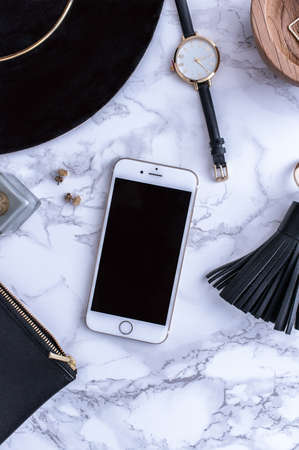 A white mug with black coffee on a white countertop. There are white meringues nearby. A phone, a black hat and black women's accessories. Top view. High quality photoの写真素材