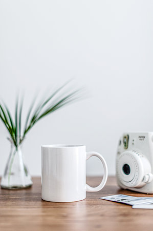 A coffee mug, a camera, green plants on a wooden surface. Side viewの写真素材