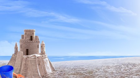 Sand castle on the seashore. Next to it is a blue plastic baby bucket and a red baby shovelの写真素材