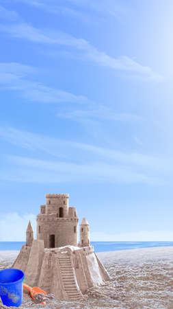 Sand castle on the seashore. Next to it is a blue plastic baby bucket and a red baby shovelの写真素材