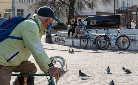 Lutsk, Ukraine - May 20,2020: Active lifestyle in the middle of coronavirus epidemic. The elderly man wearing a face mask and gloves rides a bicycle on a public streets during a quarantine in the cityのeditorial素材