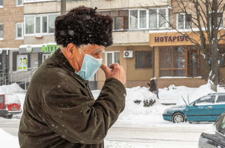 Lutsk, Ukraine - February 12,2020: Man wearing face mask on public streets in middle of coronavirus epidemic in winter. Health protection, virus outbreak prevention during infectious diseases in cityのeditorial素材