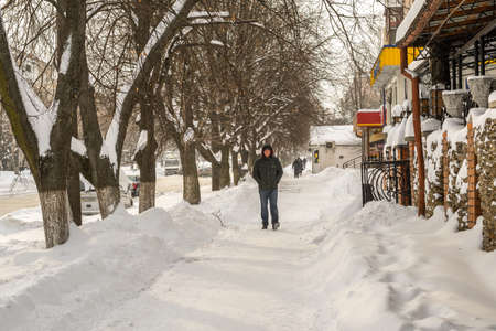 Lutsk, Ukraine - February 12,2020: People on street after snow storm. City street after blizzard. Record-breaking amounts of snow. Uncleaned slippery roads and sidewalk in winter. Cars in snowdriftのeditorial素材