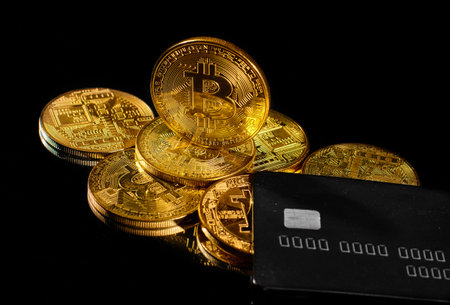 Golden coin with bitcoin logo and credit card. Leader in cryptocurrency BTC and bitcoin rewards card against black surface. Decentralized digital currency. Crypto payment. Electronic money or e-cashの写真素材
