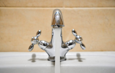 Common mixer tap. Water flowing out of bathroom stainless steel pillar tap into sink. Wasting water by leaving chrome faucet tap running. Overusing household water. Water misuse in domestic dutiesの写真素材