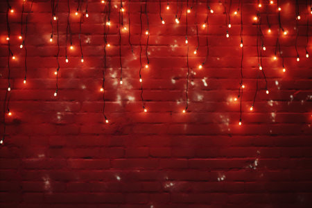 Christmas lights on red brick wall background. Christmas and New Year conceptの素材