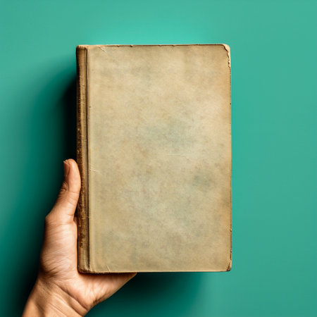 Old book in female hand on turquoise background, top viewの素材