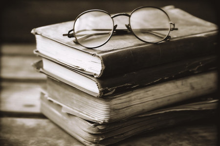 Old books and glasses on a wooden table. Black and white photo.の素材