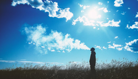 Silhouette of a man standing on a meadow and looking at the sunの素材