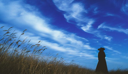 Silhouette of a woman in the grass against a blue skyの素材