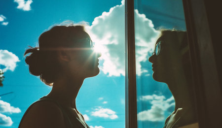 Silhouette of a young woman looking out the window on a sunny dayの素材