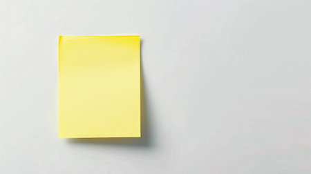 Yellow sticky note on white wall background with copy space for text.の素材